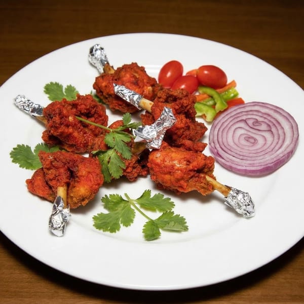 Indian chicken lollipops with foil-wrapped bones, garnished with cilantro, tomatoes, bell peppers, and red onion.