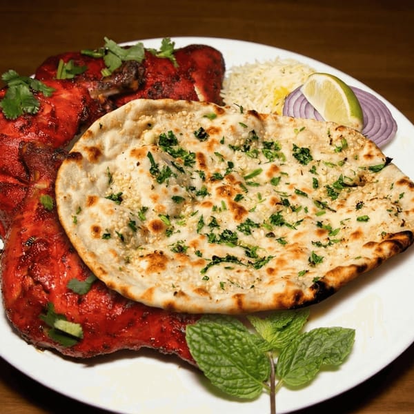 Tandoori chicken with naan, rice, red onion, lime, and mint on a white plate.